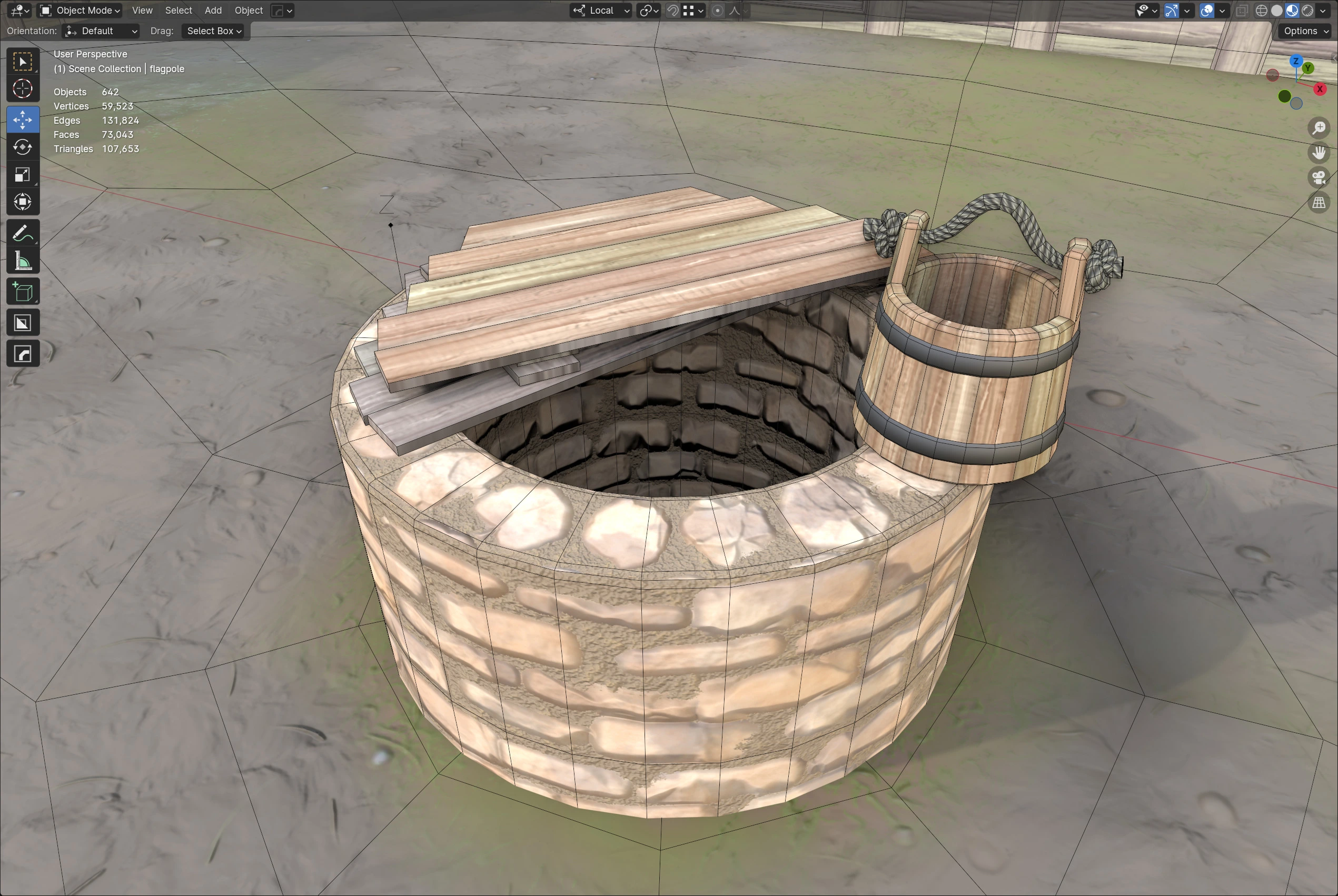 A close-up of the 3D model of a stone well with a wooden bucket, showing the detailed texturing and underlying wireframe mesh in Blender.